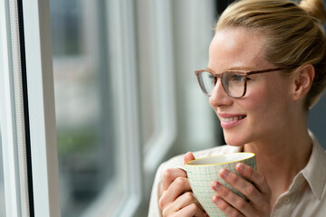 Young businesswoman with cup of coffee looking out of window