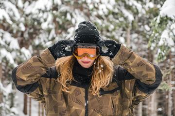 Young woman putting on ski goggles in winter forest