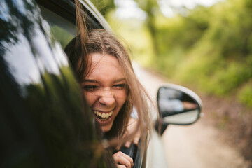 Carefree young woman leaning out of car window