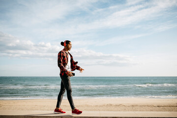 Young man walking on wall in front of the beach promenade listening music with headphones