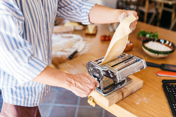 Woman rolling dough with pasta machine, partial view