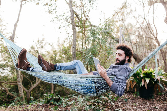 Man lying in hammock using tablet