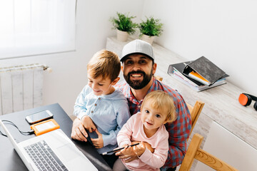 Father working at home, using laptop with his children on his lap