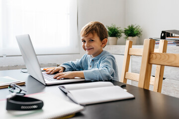 Little boy sitting in his father's office, using laptop