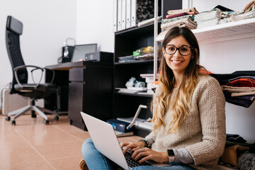 Portrait of smiling young woman sitting on the floor at home using laptop