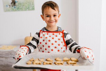 Portrait of smiling little boy holding baking tray with home-made cookies