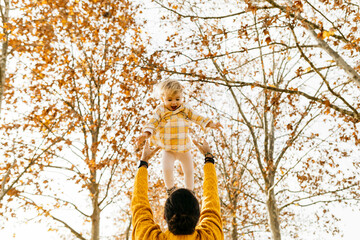 Father throwing his daughter in air, in a park in autumn
