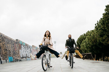 Carefree couple riding e-bikes on a promenade - obrazy, fototapety, plakaty
