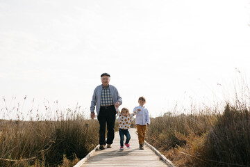 Grandfather and grandchildren strolling hand in hand on boardwalk - obrazy, fototapety, plakaty
