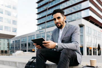 Porrait of a casual young businessman sitting on stairs in the city using tablet