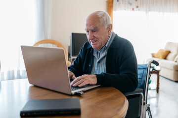 Portrait of content senior man in wheelchair using laptop at home