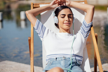 Young woman wearing headphones relaxing in a deckchair