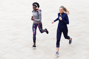 Two sporty young women running together in the city