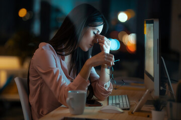 Tired young woman with eyes closed sitting at desk in office - obrazy, fototapety, plakaty