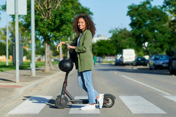 Confident young woman standing with electric push scooter on road in city