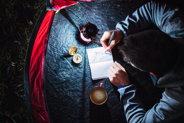 Man camping in Estonia, drawing in his sketchbook at night