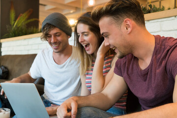 Three excited friends looking at laptop in a cafe