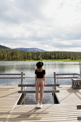 Finland, Lapland, woman wearing a hat standing on jetty at a lake