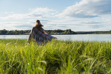 Finland, Lapland, woman wrapped in a blanket at the lakeside