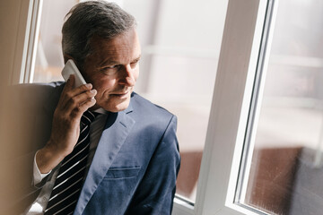 Smiling mature businessman on cell phone looking out of window