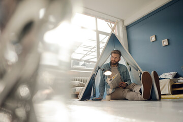 Man camping in his living room, reading the newspaper