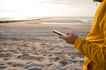 Man in yellow jacket, using smartphone on the beach