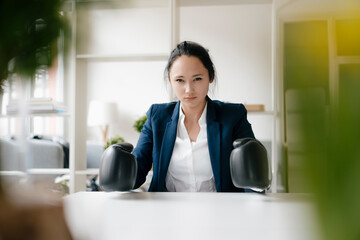 Portrait of young businesswoman sitting at desk wearing boxing gloves