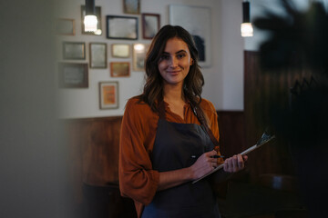 Portrait of smiling woman holding clipboard in restaurant
