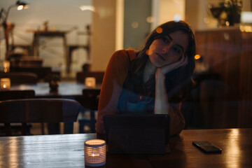 Serious young woman sitting at table in a restaurant using tablet