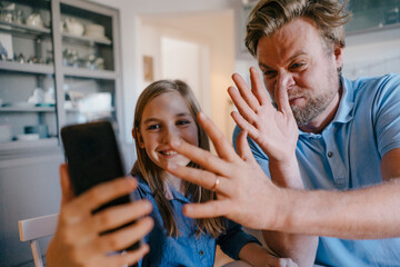 Playful father and daughter taking a selfie at home