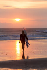 Indonesia, Bali, young woman with surfboard at sunset