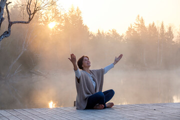 Adult woman meditating onlakeshorejetty at foggy sunrise