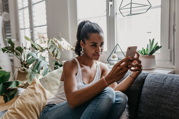Portrait of young woman sitting on the couch at home taking selfie with mobile phone