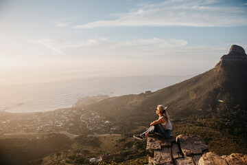 South Africa, Cape Town, Kloof Nek, woman sitting on rock at sunset