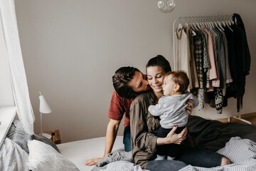 Happy family with baby girl sitting on bed at home - obrazy, fototapety, plakaty