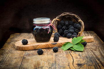 Glass of homemade blackberry jelly and blackberries on wood