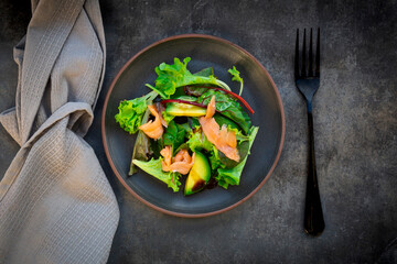 Plate of green salad with corn salad, arugula, spinach, red leaf lettuce, beetroot leaves,avocado, salmon meat and balsamic vinegar