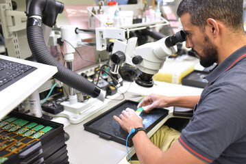 Man using a microscope for the quality control in the manufacturing of circuit boards for the...