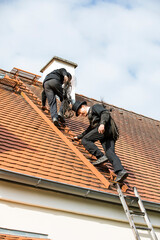 Two chimney sweeps climbing up house roof