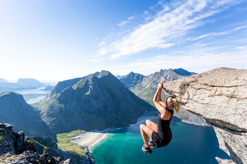 Mid adult woman hanging on edge of mountain at Ryten, Lofoten, Norway