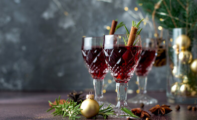 Glasses of red wine in a New Year's atmosphere, garland, lights, spices, Christmas decor. Mulled wine in glasses with rosemary and a cinnamon stick on a dark background, horizontal, copy space.