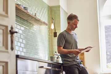 Mature man reading newspaper in kitchen at home
