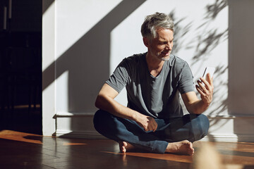 Mature man sitting on the floor at home using cell phone