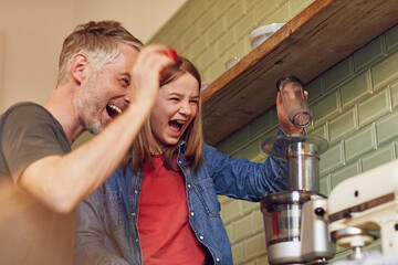 Playful father and daughter in kitchen preparing a smoothie