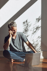 Mature man on the phone sitting on the floor at home with laptop