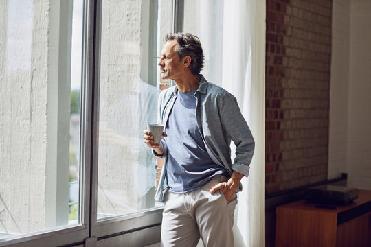 Senior man looking out of window in a loft flat