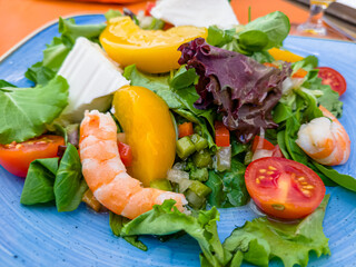 Salad with shrimp, tomatoes and feta cheese is on a plate in a restaurant