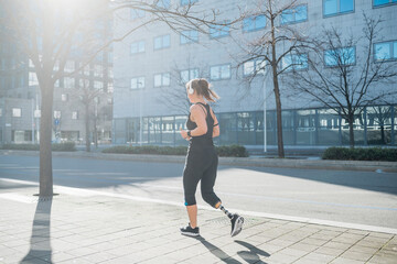 Sporty young woman with leg prosthesis running in the city