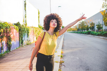 Young woman with afro hairdo hitchhiking in the city