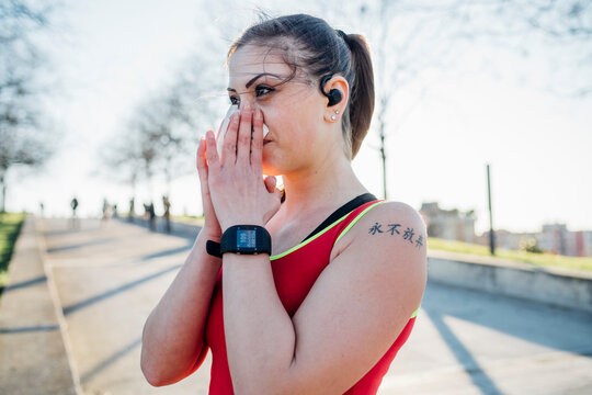 Sporty young woman with wireless earphones blowing her nose